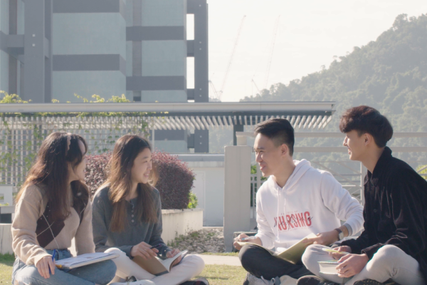 A group of students gathering on the grass in an outdoor common area. Companions are important for wellbeing!